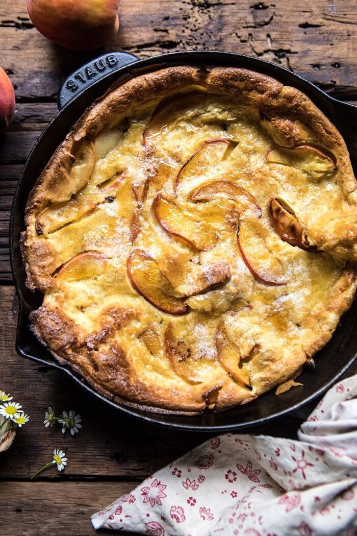 overhead photo of Browned Butter Cinnamon Peach Dutch Baby with chamomile flowers and towel