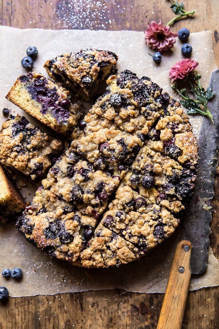 overhead photo of Bursting Blueberry Cardamom Buckle with knife and flowers in photo 