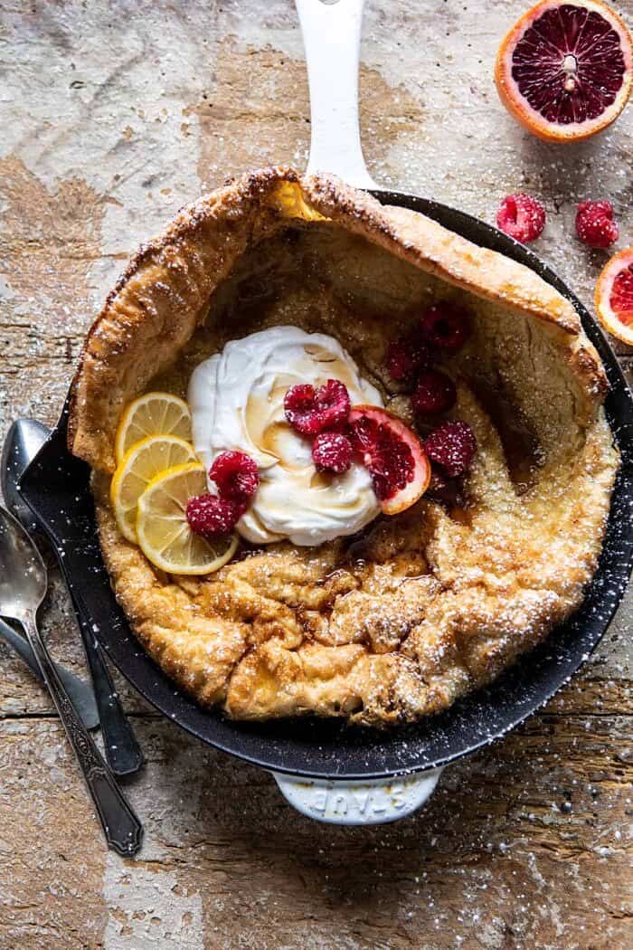 overhead photo of Whole Wheat Dutch Baby with Meyer Lemon Whipped Ricotta with spoons and berries on surface