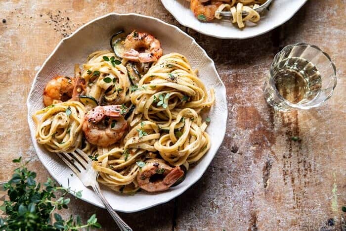 horizontal photo of Garden Herb Shrimp Scampi Linguine with fork in bowl and wine glass on table