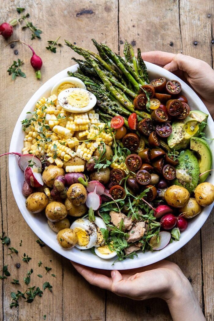 overhead photo of Summer Niçoise Salad in bowl with hand on bowl