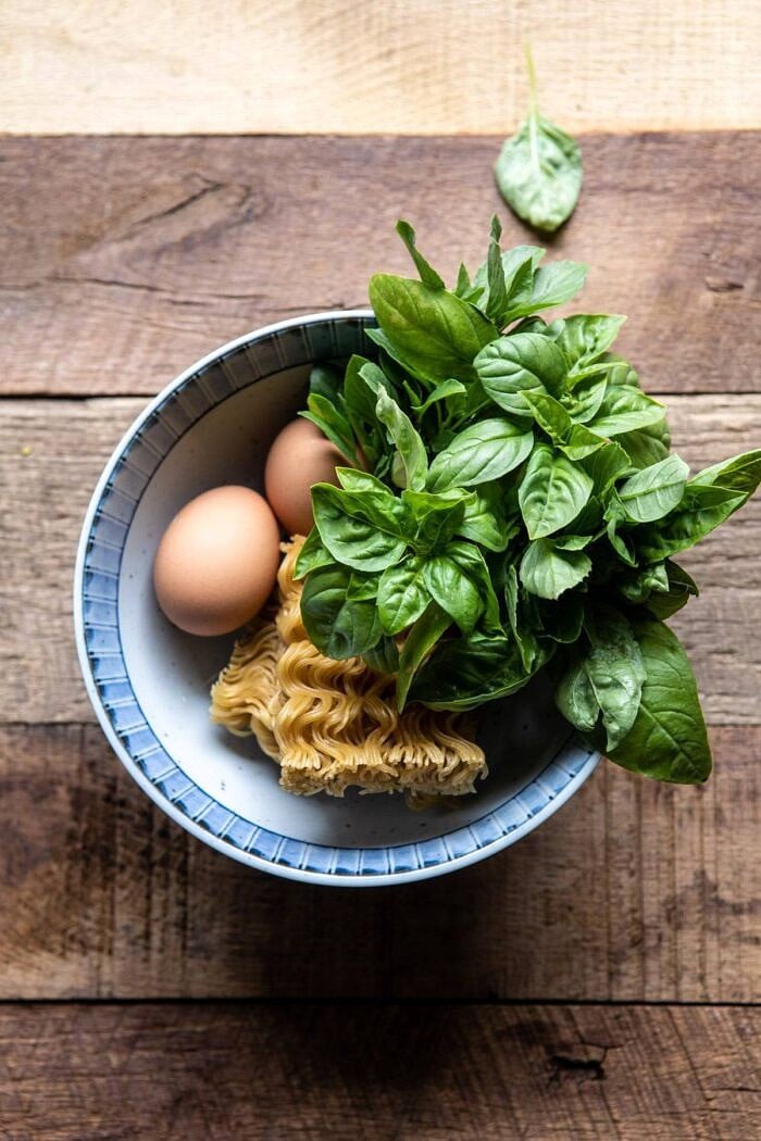 fresh basil, raw eggs, and uncooked ramen in a bowl before being prepared 