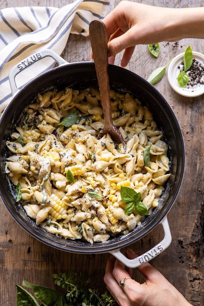 overhead photo of One Pot Lemon Basil, Corn, and Ricotta Pasta with hands on pot and wooden spoon in pot 