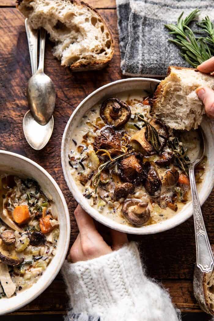 overhead photo of Creamy Wild Rice Chicken Soup with Roasted Mushrooms in soup bowls with hands on bowl and bread in soup