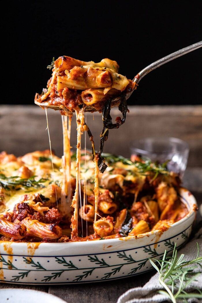 side angled photo of One Pot Spicy Pesto Cheese Baked Rigatoni with spoon pulling up pasta and cheese pulling 