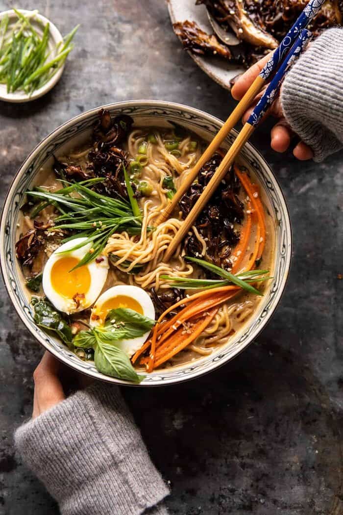 overhead photo of 30 Minute Creamy Sesame Miso Ramen with Crispy Mushrooms and hands on soup bowl pulling noodles up