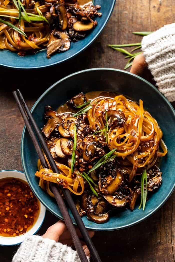 overhead photo of 30 Minute Saucy Ginger Sesame Noodles with Caramelized Mushrooms with hands on bowl 