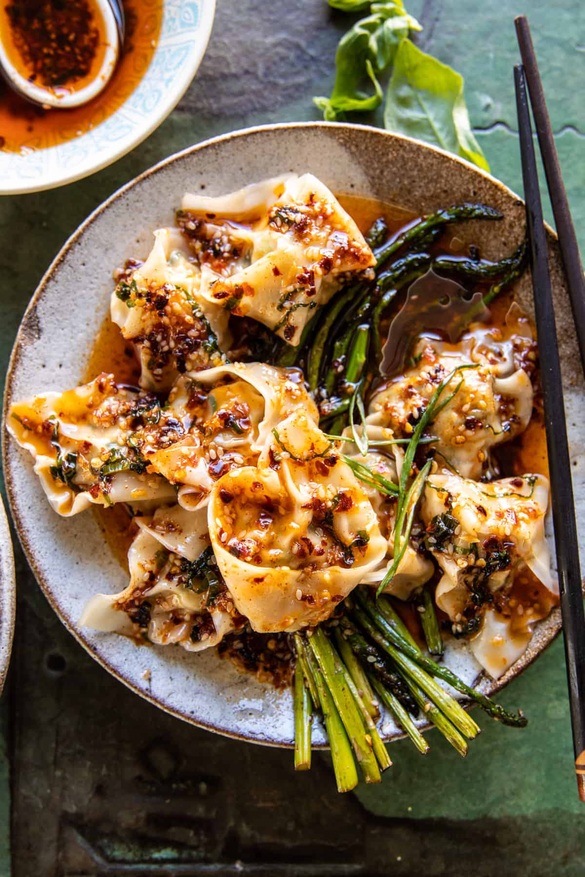Quick Wontons in Chili Oil with Asparagus on a plate with chopsticks and extra chili oil on the side 