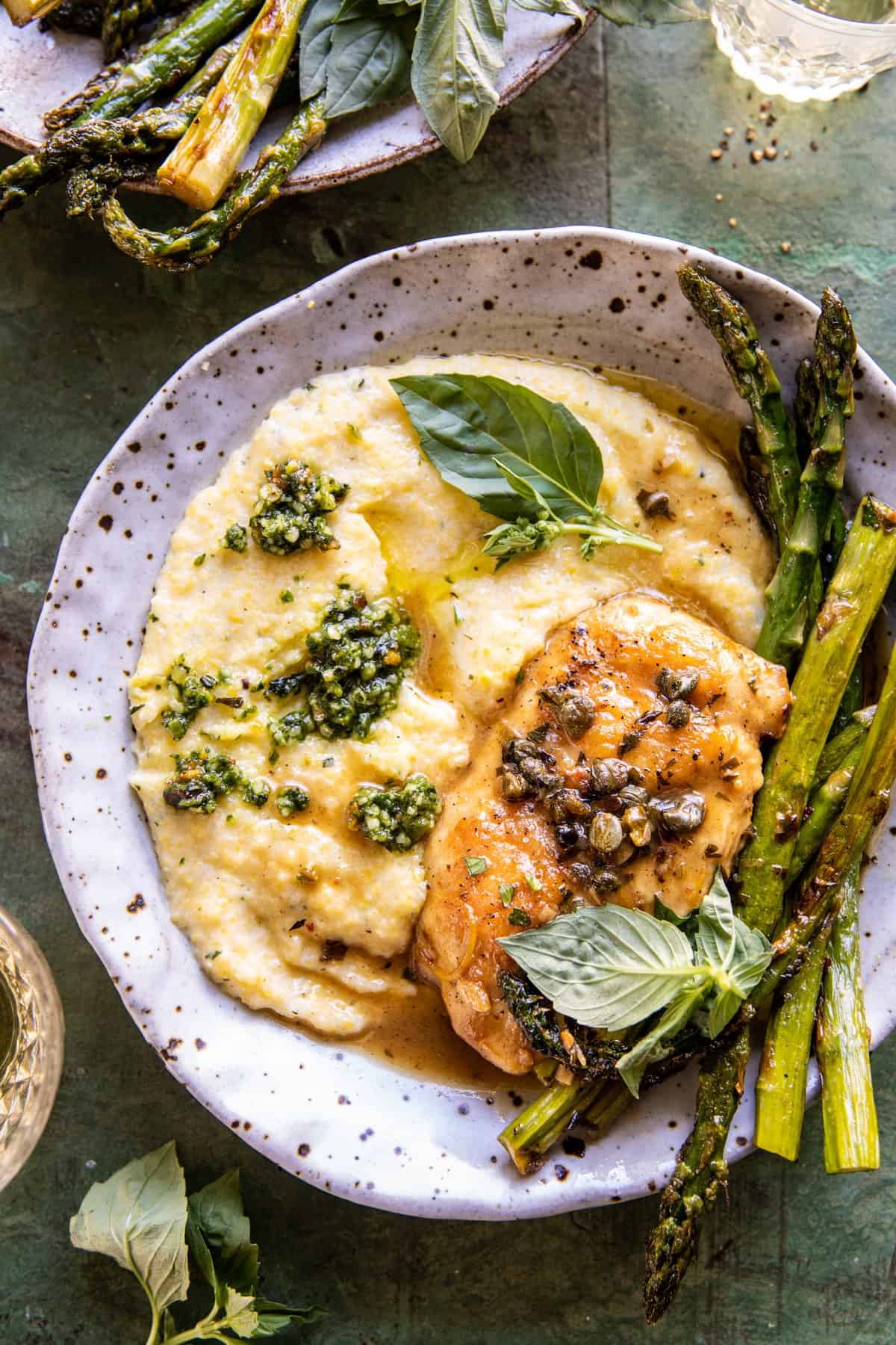 chicken on a plate with polenta and asparagus. wine one the table 